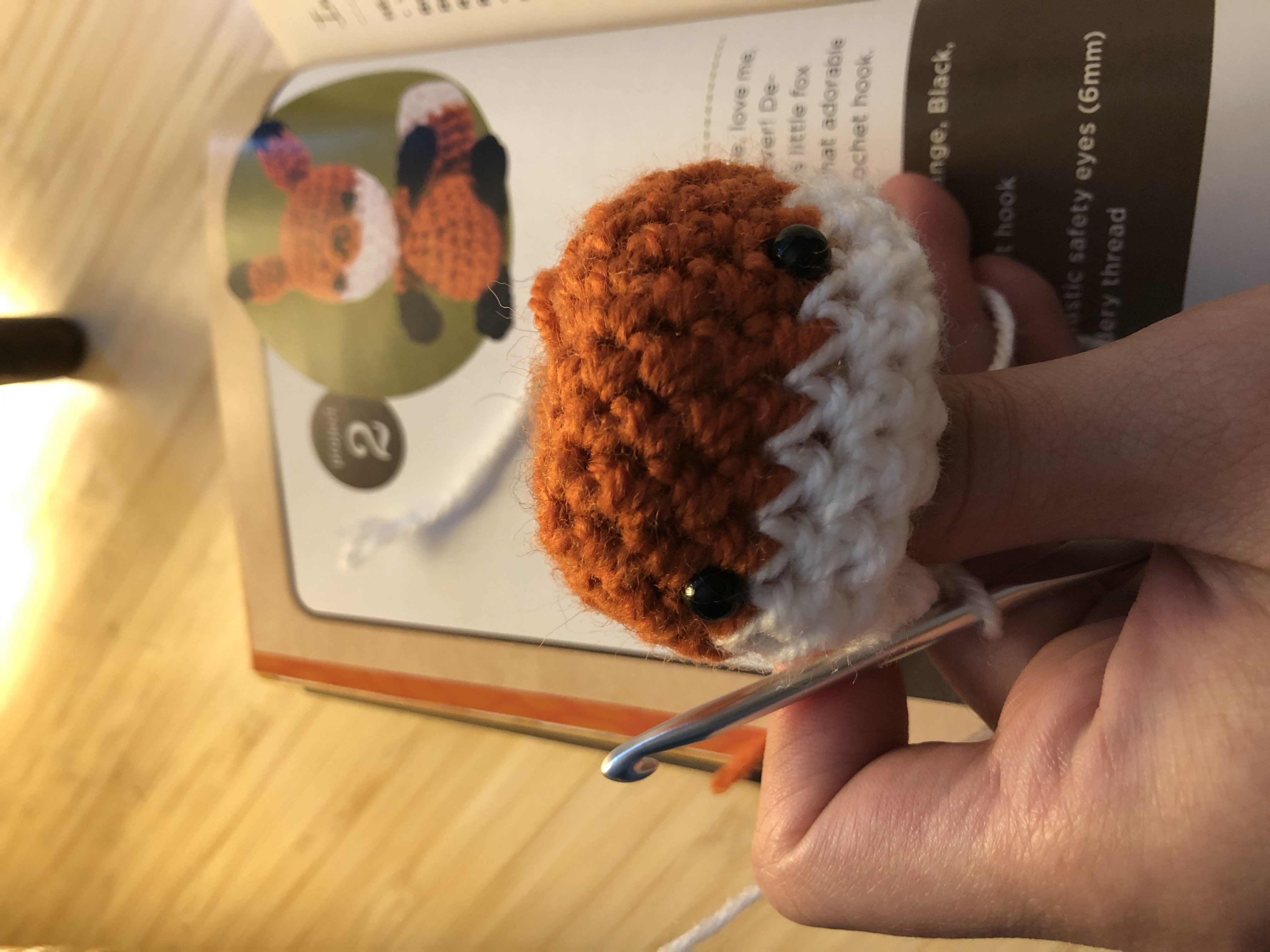 A complete rounded head of the amigurumi fox with eyes attached but no ears